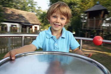 Porträt eines lächelnden kleinen Jungen auf einem Karussell auf einem Spielplatz - RDF001230