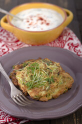 Bowl of yoghurt dip with garlic and mint and a plate with zucchini fritters, studio shot - ODF000636
