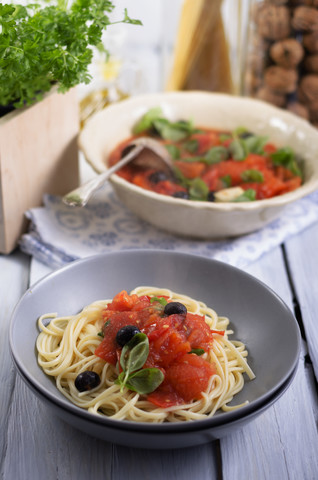 Spaghetti mit Soße aus gegrillten Tomaten mit schwarzen Oliven und Basilikumblättern, Studioaufnahme, lizenzfreies Stockfoto