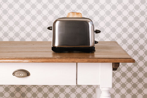 Alter Küchentisch mit Toaster und Brotscheibe vor einer Ornamenttapete, Studioaufnahme - DRF000269