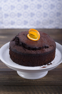 Schokoladenkuchen garniert mit Orangenscheibe auf Kuchenständer auf Holztisch, Studioaufnahme - ODF000658