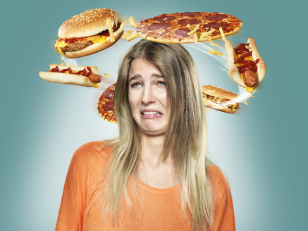 Angewiderte junge Frau mit fliegendem Fastfood um den Kopf, Composite - STKF000502