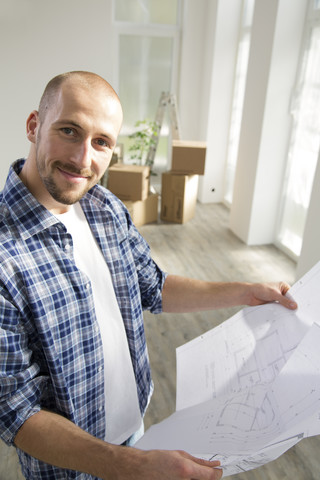 Junger Mann in neuem Haus mit Bauplan, lizenzfreies Stockfoto