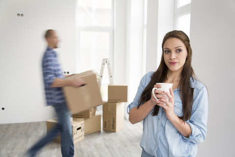 Junges Paar zieht in ein neues Haus ein, Frau hält eine Tasse Kaffee, lizenzfreies Stockfoto