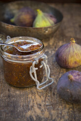 Four figs (Ficus carica), a bowl and a glass of fig jam on wooden table, studio shot - LV000309