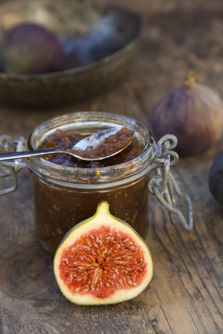 Sliced fig, whole figs (Ficus carica) and a glass of fig jam on wooden table, studio shot stock photo
