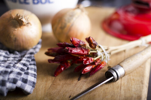 Getrocknete rote Chilischoten, Zwiebeln und ein Messer auf einem hölzernen Schneidebrett - ODF000679