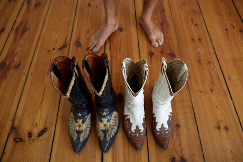 Germany, Berlin, Cowboy boots on wooden floor, bare feet in background - TKF000220