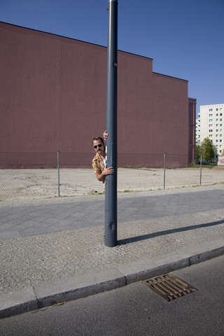 Deutschland, Berlin, Mann guckt hinter Laternenmast hervor, lizenzfreies Stockfoto
