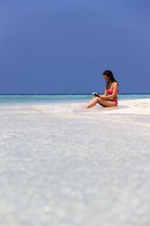 Malediven, Junge Frau im Bikini sitzt im seichten Wasser und liest ein Buch - AMF001214