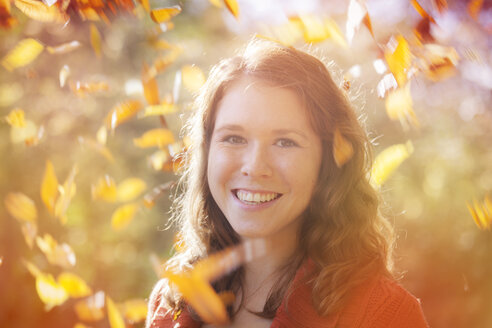 Porträt einer glücklichen jungen Frau mit wirbelnden Herbstblättern um sie herum, Nahaufnahme - BGF000006
