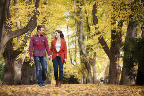 Glückliches junges Paar, das Hand in Hand in einem Park spazieren geht - BGF000018
