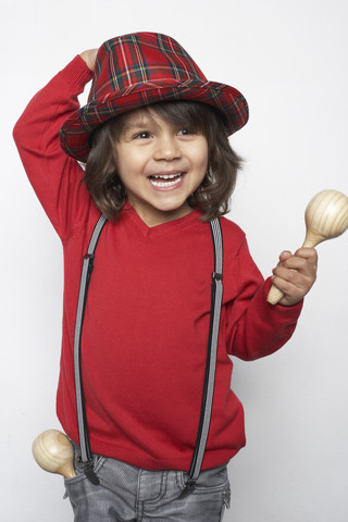 Porträt eines lächelnden kleinen Jungen mit Holzrassel, der Hut und Hosenträger trägt, lizenzfreies Stockfoto