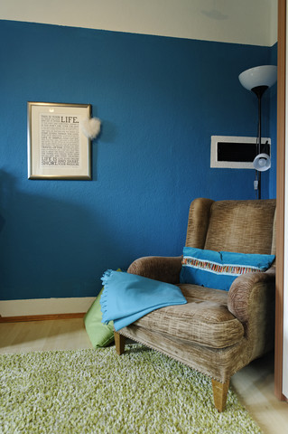 Wing chair standing in a corner of a living room in front of blue coloured wall stock photo