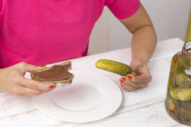 Junge Frau isst Essiggurke und Scheibe Brot mit Schokoladencreme - DRF000285