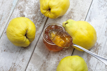 Four quinces (Cydonia oblonga), a spoon and a glass of quince marmalade on wooden table - CSF020330