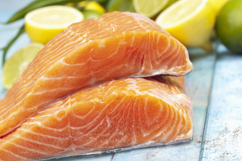 Lachsfilets (Salmo salar) und Zitronen auf blauem Holztisch, lizenzfreies Stockfoto