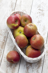Äpfel (Malus) in weißem Korb auf Holztisch - CSF020347