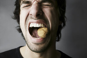 Portrait of young man trying to crack a walnut with his teeth, studio shot - JATF000518