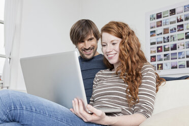 Germany, Munich, Couple sitting on sofa using laptop - RBF001429