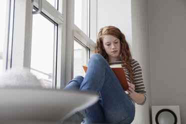 Deutschland, München, Frau sitzt auf der Fensterbank und liest ein Buch - RBF001432