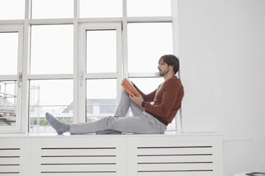 Deutschland, München, Mann liest Buch, sitzt auf Fensterbank - RBF001489