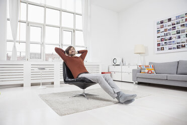 Germany, Munich, Man at home, sitting in chair, hands behind head - RBF001455