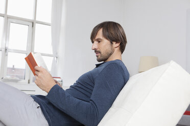 Germany, Munich, Man sitting on sofa, reading book - RBF001491