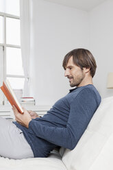 Germany, Munich, Man sitting on sofa, reading book - RBF001462