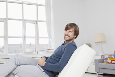 Deutschland, München, Mann sitzt auf Sofa, lächelnd - RBF001464