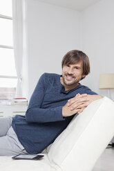 Germany, Munich, Man sitting on sofa, smiling - RBF001465