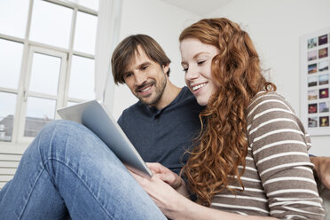 Germany, Munich, Couple sitting on sofa using digital tablet - RBF001483