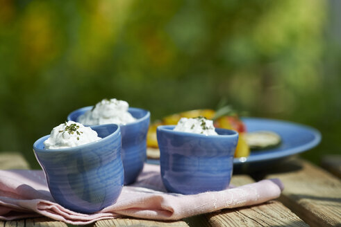 Bowls of curd with herbs on garden table - SRSF000405