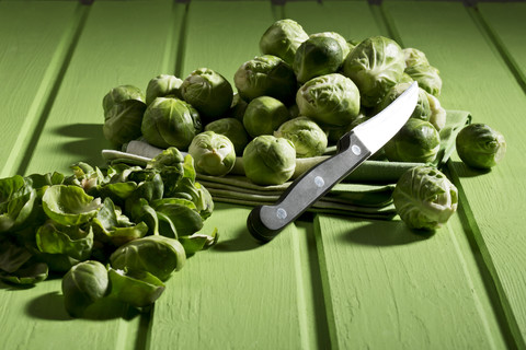 Rosenkohl auf Küchenhandtuch, Messer auf grünem Holztisch, lizenzfreies Stockfoto