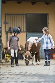 Germany, NRW, Korchenbroich, Boy and Girl at riding stable with mini shetland pony - CLPF000010