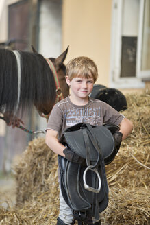 Germany, NRW, Korchenbroich, Boy holding saddle - CLPF000008