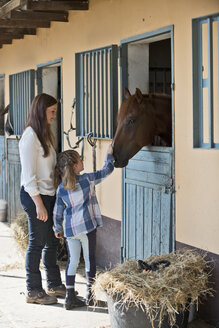 Germany, NRW, Korchenbroich, Woman and girl stroking horse in stable - CLPF000004