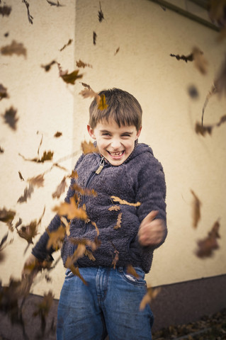 Grinning little boy throwing autumn leaves stock photo