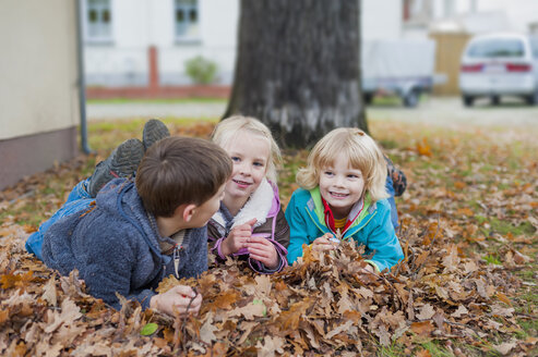 Drei Kinder liegen im Herbstlaub - MJF000414