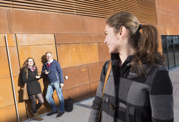 Junge Frau schaut auf zwei Studenten im Hintergrund - DISF000241