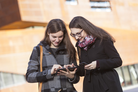 Zwei junge Frauen benutzen ein digitales Tablet im Freien, lizenzfreies Stockfoto