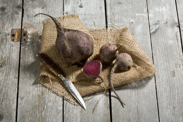 Sliced and whole beetroots (Beta vulgaris), jute and knife on wooden table - MAEF007440