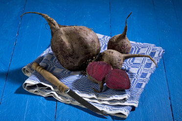 Geschnittene und ganze Rote Beete (Beta vulgaris), Tuch und Messer auf blauem Holztisch - MAEF007441