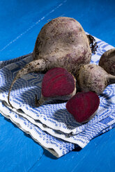 Sliced and whole beetroots (Beta vulgaris) and cloth on blue wooden table - MAEF007442