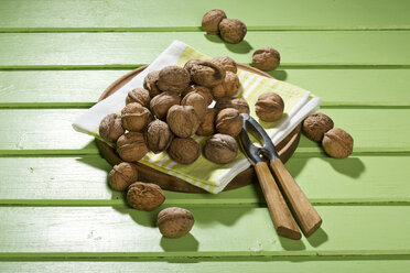 Walnüsse (Juglans regia), Nussknacker und Serviette auf grünem Holztisch - MAEF007453