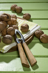 Walnüsse (Juglans regia), Nussknacker und Serviette auf grünem Holztisch - MAEF007454