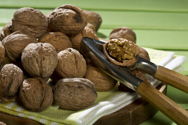 Walnuts (Juglans regia), nutcracker and napkin on green wooden table, close-up - MAEF007455