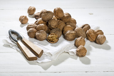 Walnuts (Juglans regia), nutcracker and dish towel on white wooden table - MAEF007457
