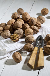 Walnüsse (Juglans regia), Nussknacker und Geschirrhandtuch auf weißem Holztisch - MAEF007458