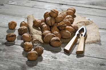 Walnuts (Juglans regia), nutcracker and burlap on wooden table - MAEF007461